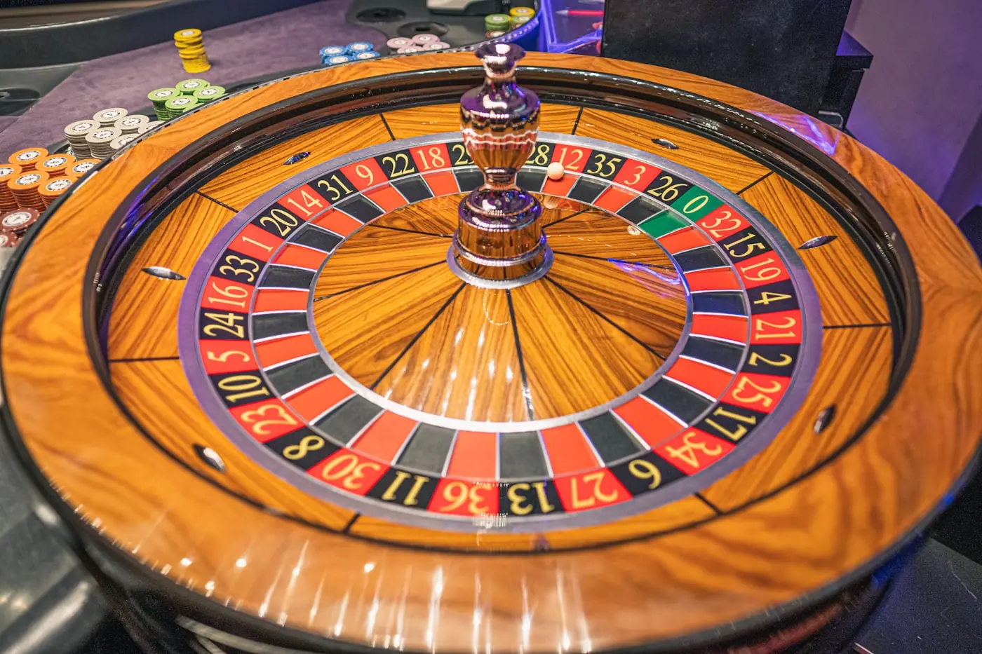 Roda roulette dengan bola kecil di atasnya dalam sorotan meja kasino.