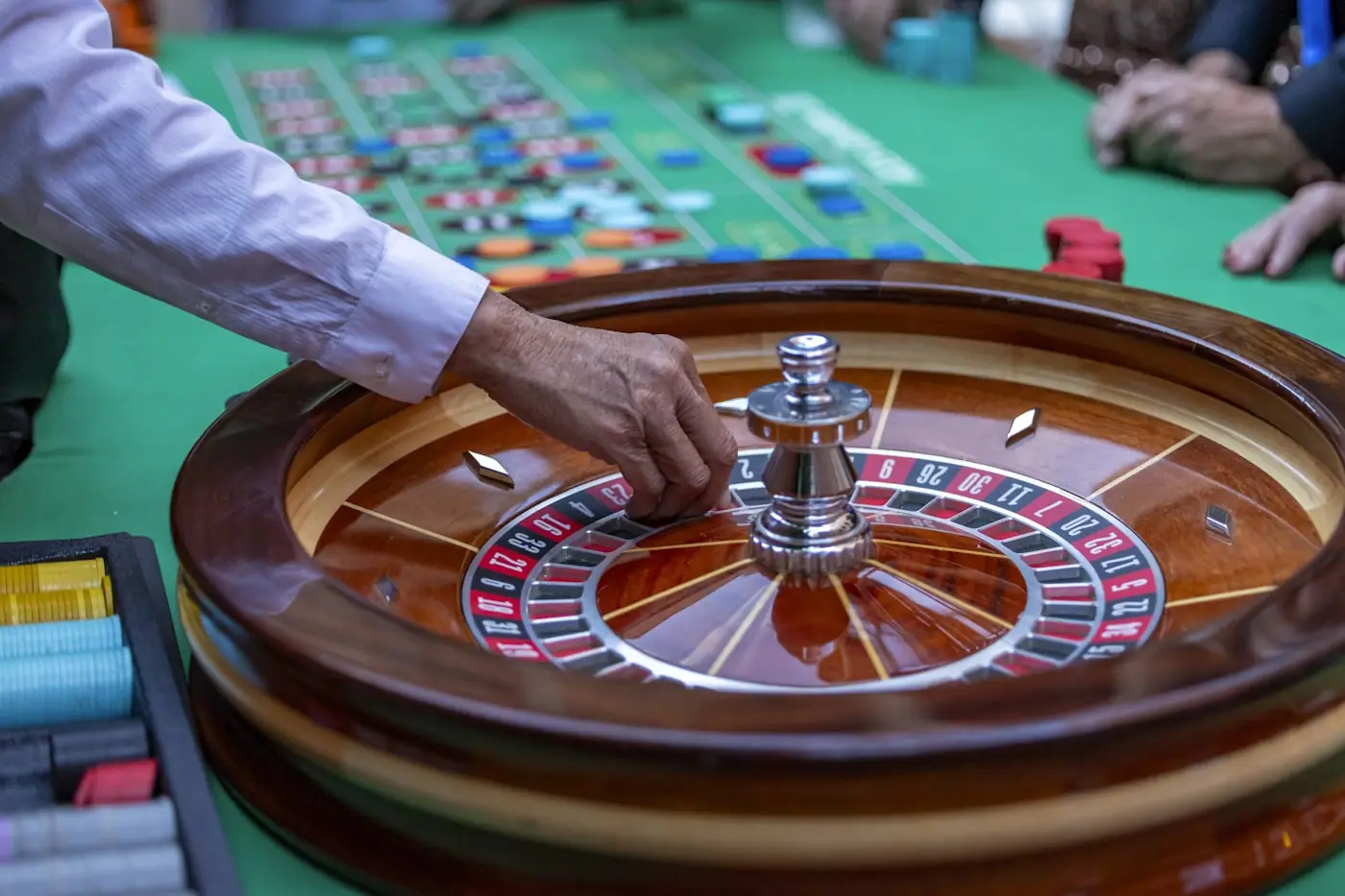 Pemain duduk di meja roulette dengan dealer di sisi meja berwarna hijau.